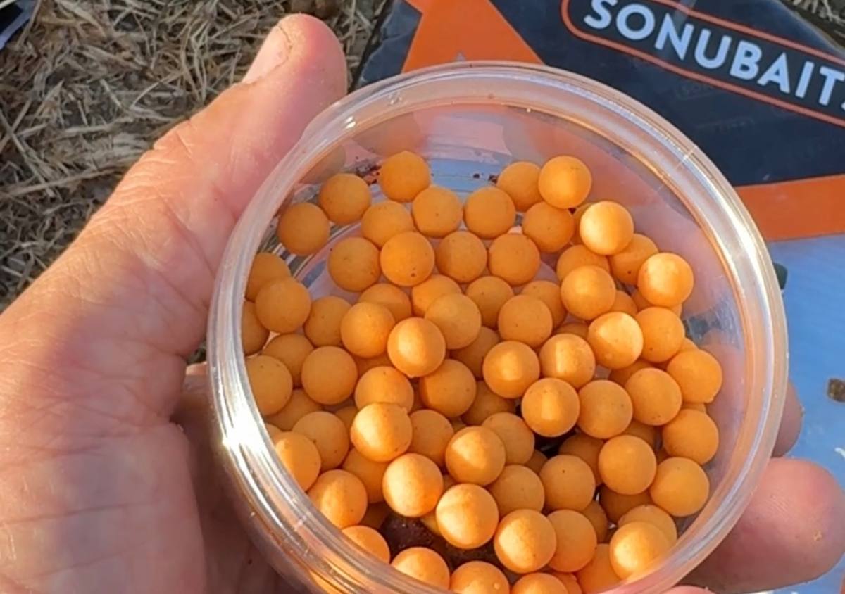 An open tub of orange wafters held in a hand with Sonubaits packaging behind it