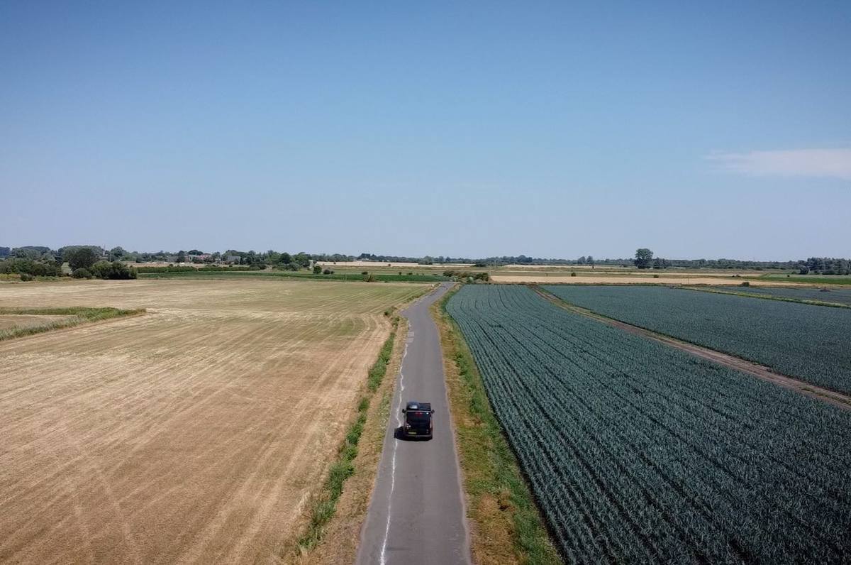 Aerial view of a dark vehicle on a narrow country road between harvested fields and green crops