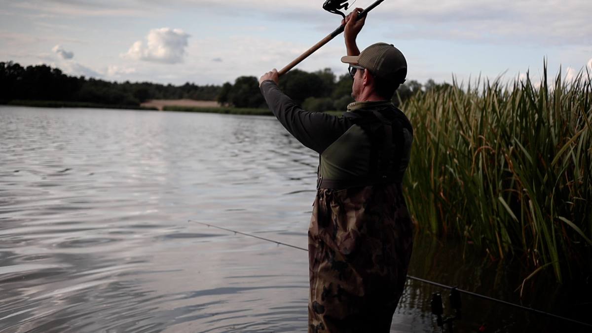 An angler holding a good-sized tench by the unhooking mat.